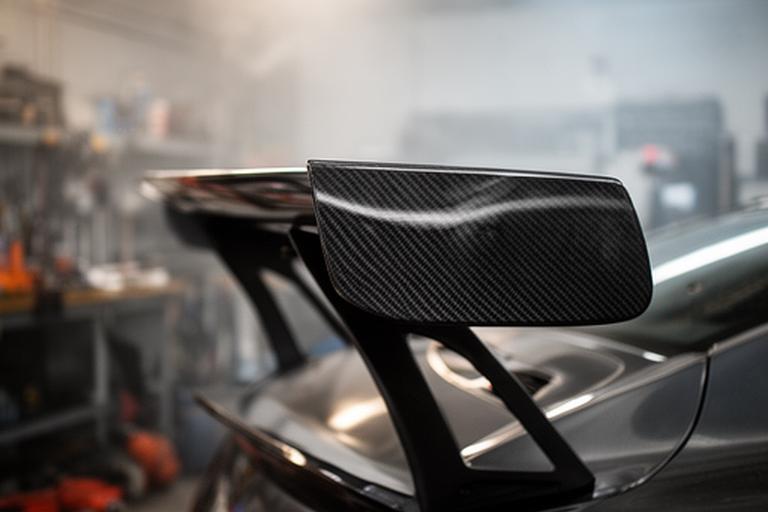 Spoiler trasero de fibra de carbono instalado en un auto de competición dentro de un taller con herramientas al fondo